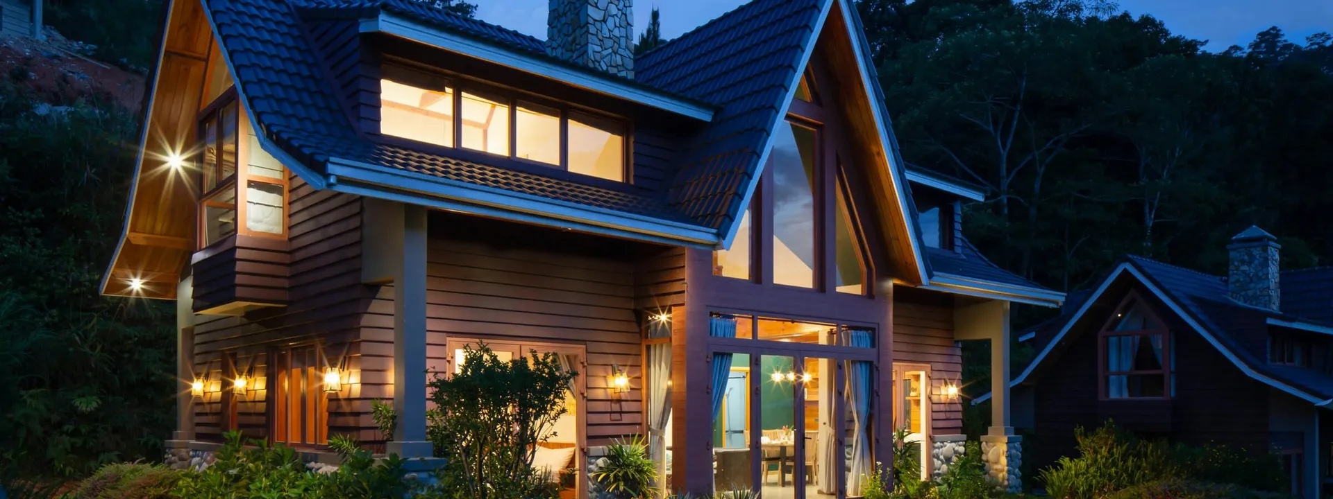 Wood-and-stone residence lit from within at dusk